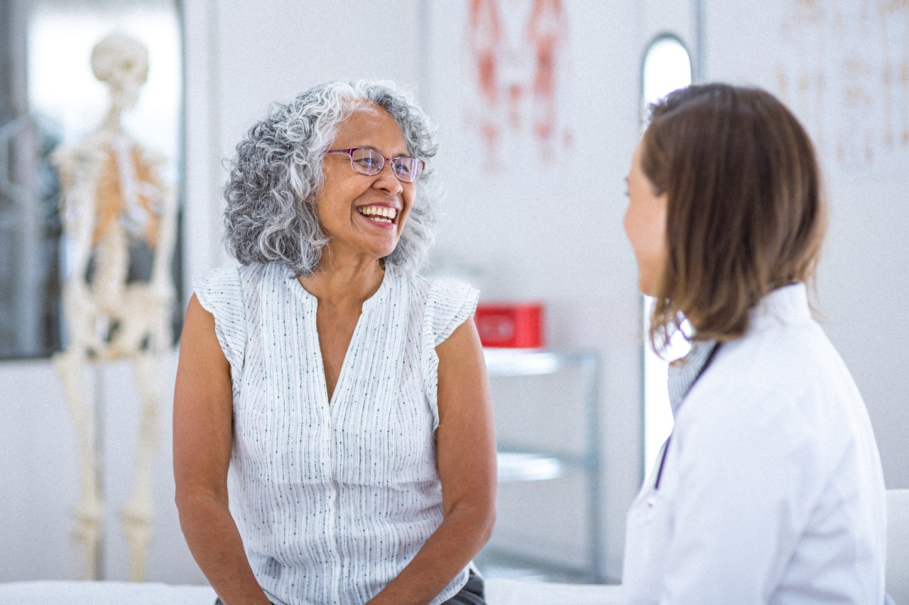 A vibrant and healthy senior woman of Hawaiian and Chinese descent smiles while talking with her female physician during a routine medical appointment.